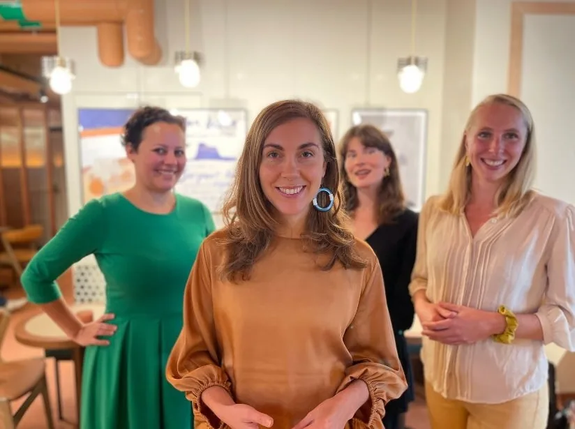 Fyra leende kvinnor från Aumla står tillsammans i en ljus lokal